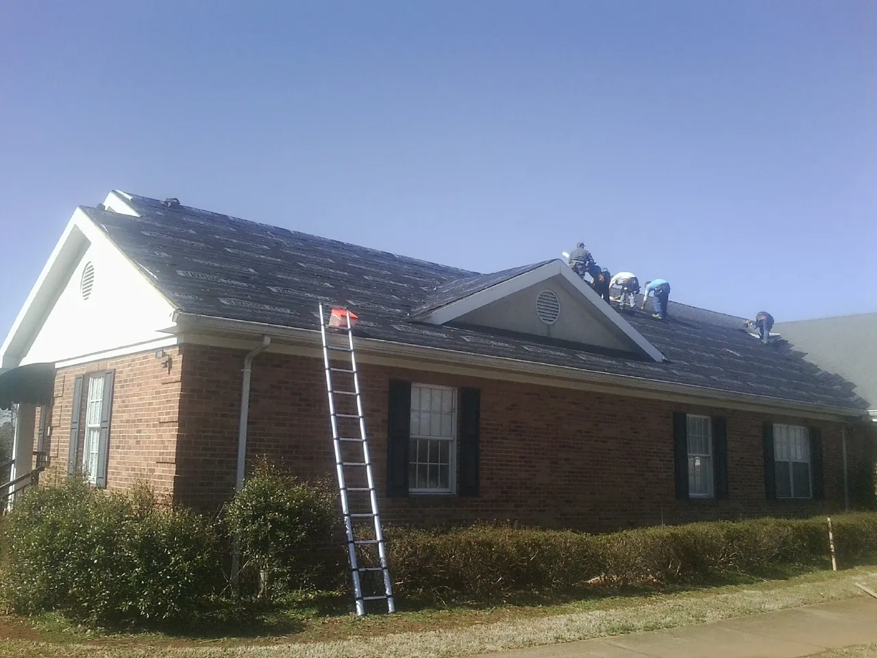 Crew tearing shingles off a brick ranch roof with a ladder set — Metal Roof Repair work by our crew in Fallbrook