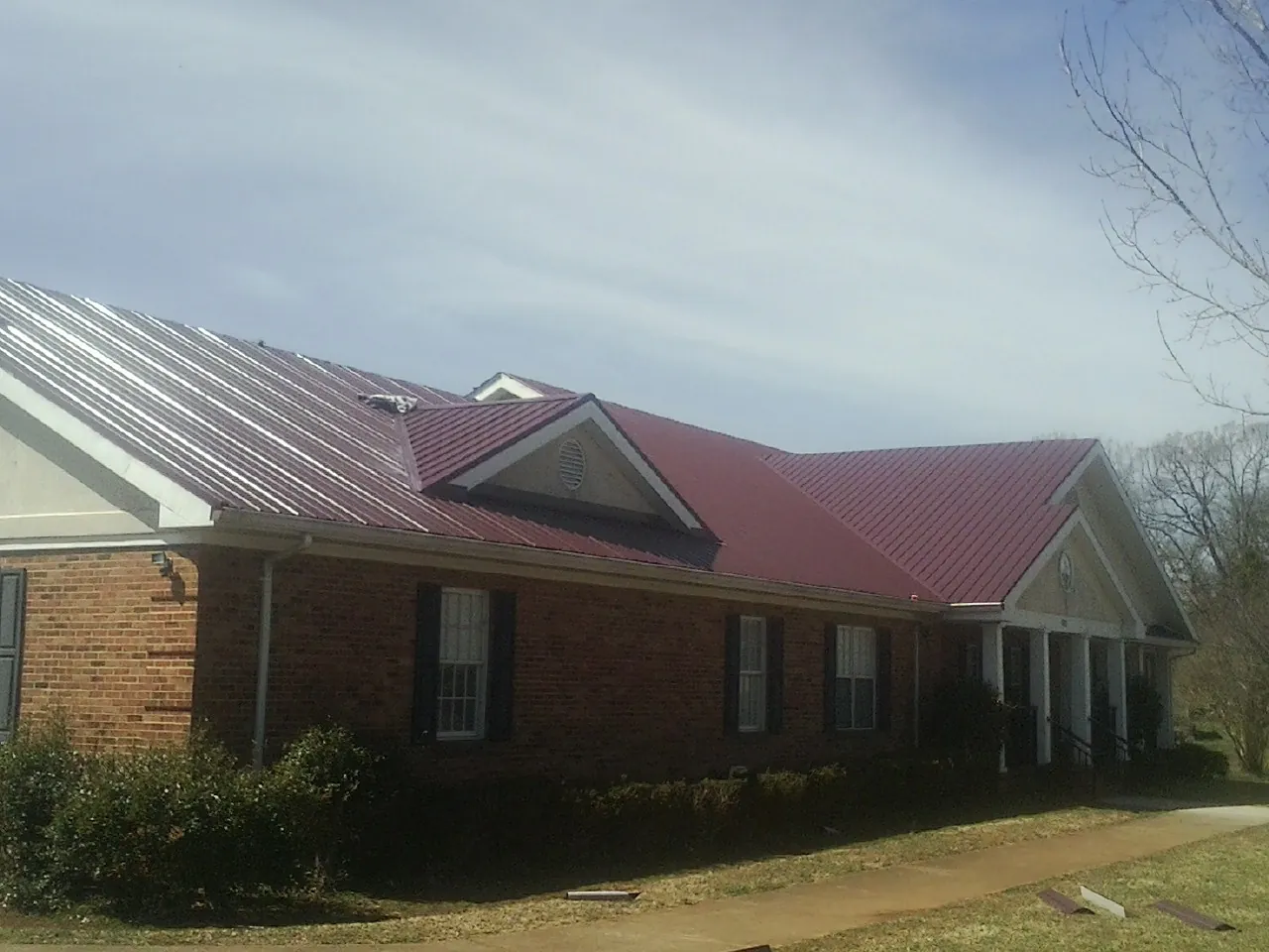 Red metal roof with gabled entries on a long brick building, from a Hail Damage Roof Repair job in Fallbrook