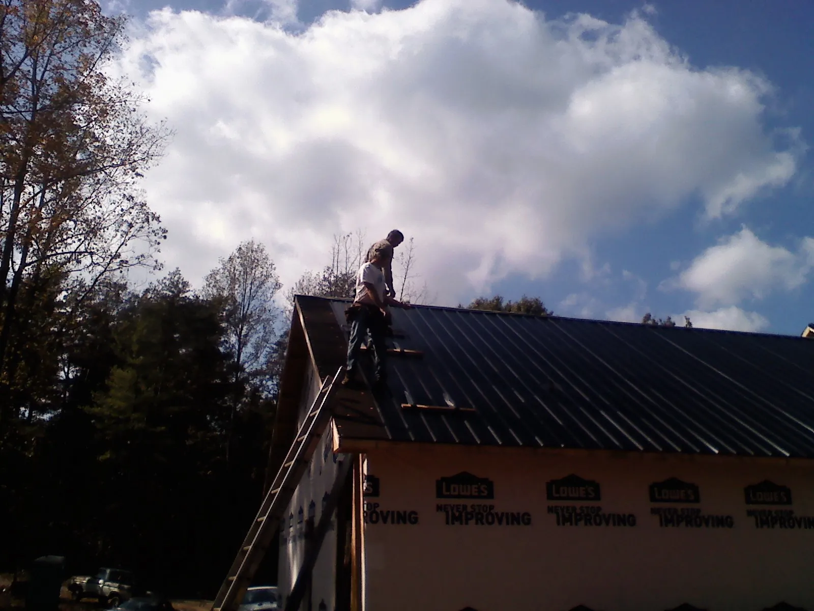 Roofer fastening dark metal panels high against a cloudy sky, from a Roof Inspection job in Fallbrook