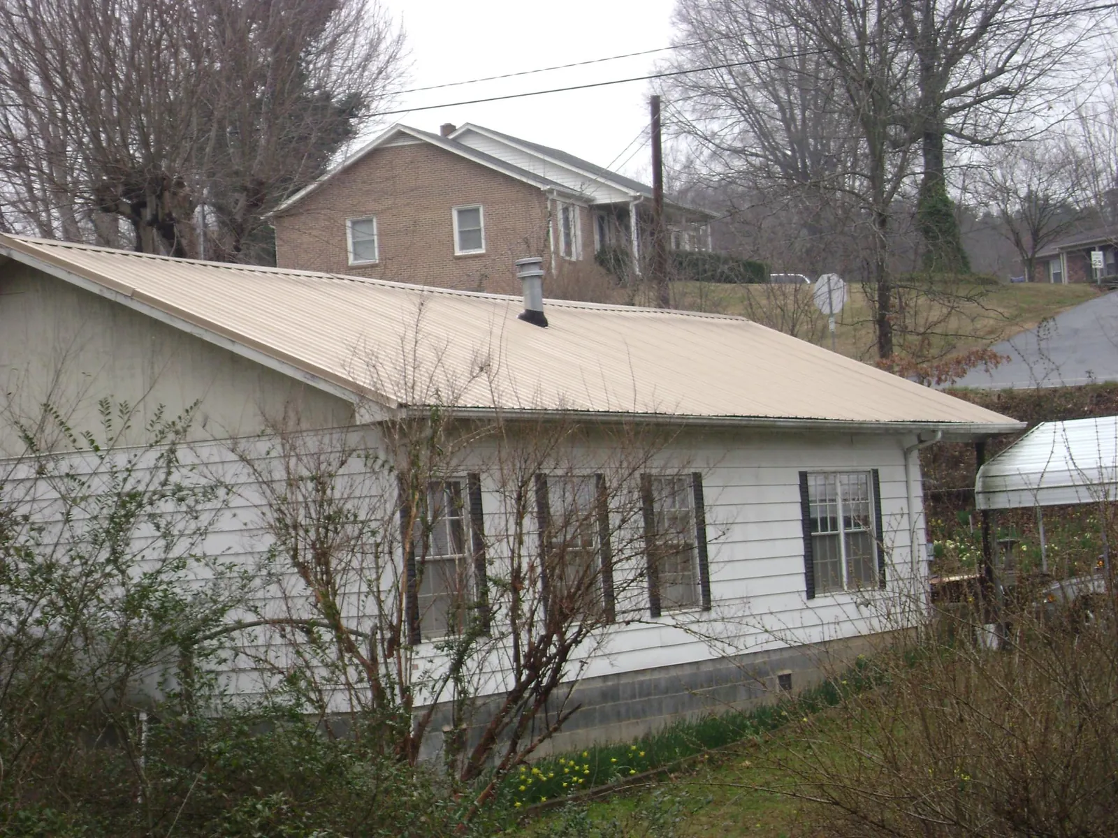 Tan metal roof on a white sided house set into a hillside — Commercial Roofing by Roofing Brothers in Fallbrook